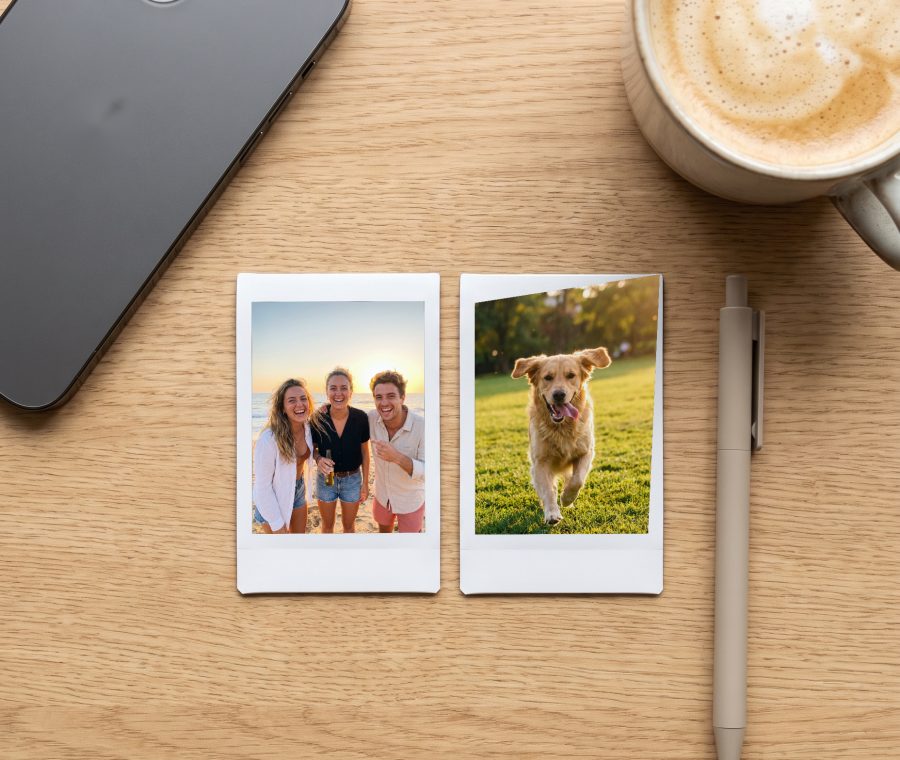 Two Instax Mini prints at real size on a desk next to an iPhone and a latte